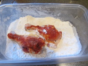 Seasoned chicken pieces being dredged in flour.